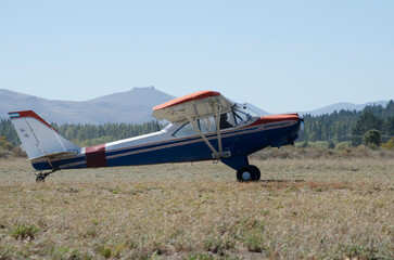 small plane on dirt runway in field, taxiing to take off. white blue and red, propeller light...