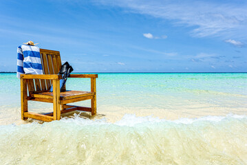 A wooden chair standing in the Indian Ocean with a towel, shell and flippers.