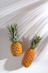 Juicy pineapple on a white background. A whole pineapple and a cut off half. Palm tree shade, creative lighting.