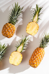 Juicy pineapple on a white background. A whole pineapple and a cut off half. Palm tree shade, creative lighting.