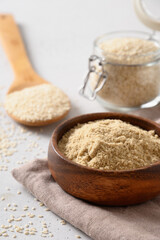 Sesame flour in wooden bowl and seeds in glass jar on white background. Vertical. Close up.