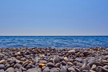 A black pebbles beach with blue sea and sky. Space for your text and logo.