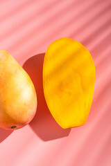 Juicy ripe yellow Thai mango on a pink background. Hard light and shadow from a palm tree.