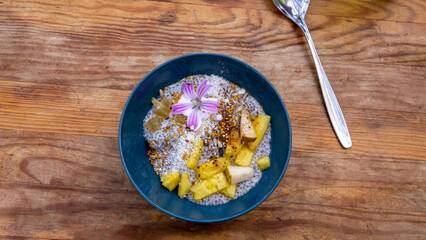 Organic vegan breakfast chia bowl with fruits, supplements, seeds, coconut, pineapple, pears. Top view against wooden rustic background. Close up.