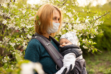 Mother in medical mask with little son in the park walk near the blooming tree