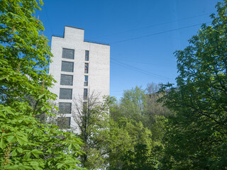 An old soviet residential building in green trees with beautiful blue sky behind. Close-up.
