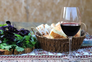 Glass of red wine, a wooden basket with bread and green herbs
