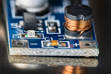 Electronic coil on blue PCB detail with reflection on shiny black background. Closeup of components...