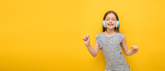 Beautiful happy little girl with closed eyes in listening to music in headphones and dancing on a...