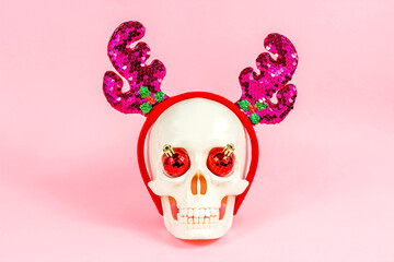 White skull with party deer horns and xmas ball decorations on light pink background. Christmas and New Year celebration concept.