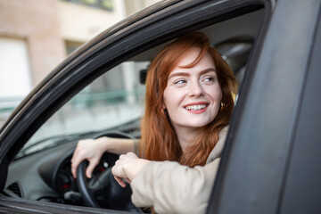 Fototapeta na wymiar Joyful redhead woman inside of car looking back from driver seat while driving during the day.