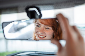 Woman hand adjusting rear view mirror of her car. Happy young woman driver looking adjusting rear view car mirror, making sure line is free visibility is good