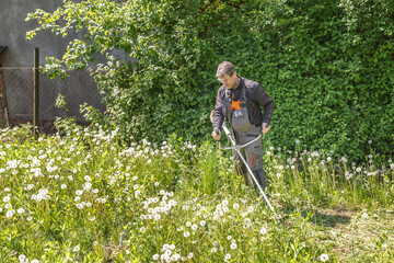 A man mows grass on his property with a gasoline trimmer