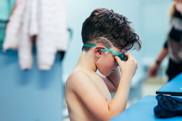 elementary caucasian boy puts on swimming goggles