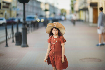 Cute girl child teenager in dress and hat on the sidewalk on city street, summer time