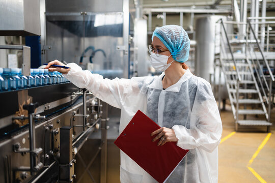 Female Worker With Protective Face Mask Working In Medical Supplies Research And Production Factory And Checking Canisters Of Distilled Water Before Shipment. Inspection Quality Control.