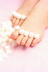 The concept of epilation, waxing. Sugar cubes lying down in a row on female feet, toes over pink background