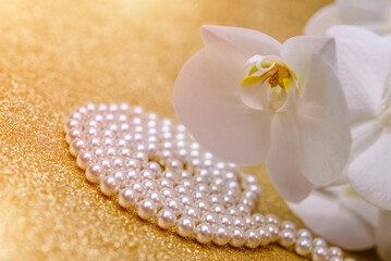 white Orchid and pearl necklace on a shiny gold background