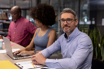 Portrait of caucasian businessman sitting besides biracial businesswoman at modern workplace