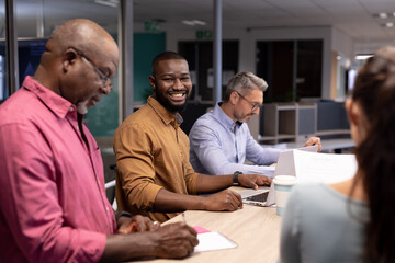 Portrait of smiling young african american businessman working amidst colleagues in modern office