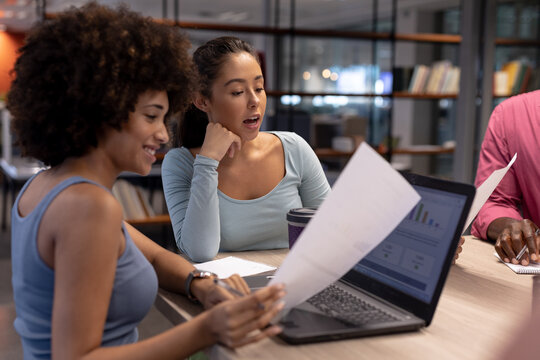 Biracial businesswomen discussing over laptop and document together during meeting at workplace