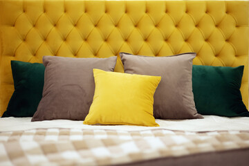 Square pillows of various colors and sizes lie on the bed with a soft yellow velvet headboard with...