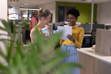 Happy multiracial female advisors with drink and document working together at modern office