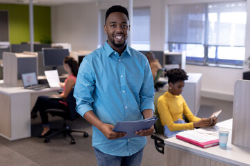 Portrait of smiling young african american businessman holding file at modern workplace