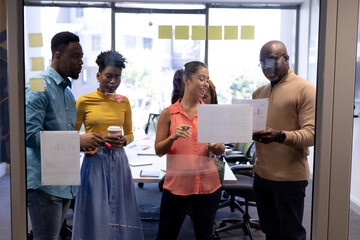 Multiracial male and female advisors planning strategy over documents seen through glass wall