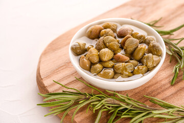 White bowl with pickled capers served with rosemary on wooden cutting board, white table background with copy space - traditional Italian antipasti