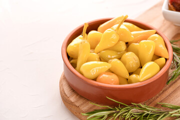 Brown bowl with pickled baby peppers served with rosemary on wooden cutting board, white table background with copy space - traditional Italian antipasti