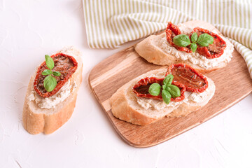 Bruschettas with ricotta cheese, sliced sun dried tomatoes topped with basil on wooden serving board, white stone table background. Classic italian antipasti