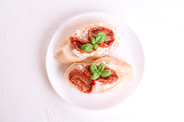 Top view on bruschettas or toasts with ricotta cheese and sun dried tomatoes topped with basil on white plate, white table background. Delicious classic italian appetizer, traditional antipasti