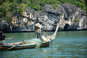 Thai man fisher people sailing wood long tail boat fishery floating in sea use net catch fishing marine and fish in ocean at Mu Ko Petra National Park at Pak Bara on April 12, 2022 in Satun, Thailand