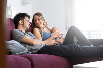 A couple of parents sitting on a sofa in the living room with their newborn baby