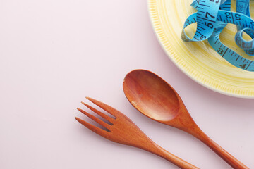 Clean plate with measurement tape and cutlery on wooden background