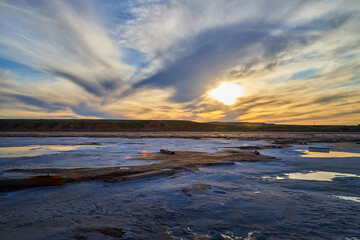 Obraz premium The shore of salt lake with puddles of water and sand, an endless horizon, a blue sky with white clouds and a large German Shepherd dog or an Eastern European Shepherd dog in the evening at sunset