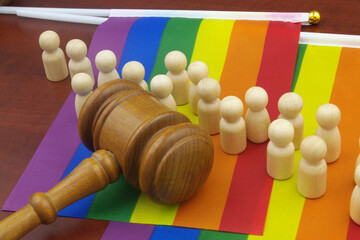 Laws and gay pride parade concept. Judge gavel and wooden people figures on LGBT flag.	