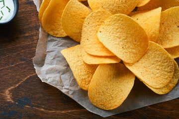 Potato corrugatedchips. Fast food. Crispy potato chips ceramic black bowl with sour cream sauce and onions in wooden stand on old kitchen table wooden background. American tradition. Hot BBQ. Top view