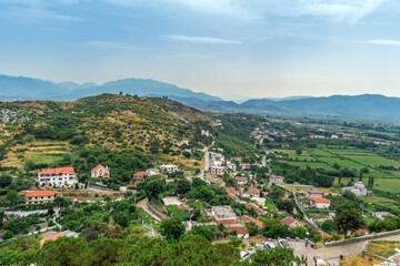 Fototapeta na wymiar Aerial view of the countryside among the mountains in the suburbs of Shkoder, Albania. Rural buildings with red roofs among the summer greenery near the hill