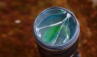 Damaged glass protective UV filter, broken protective glass filter on DSLR camera closeup. Camera lens fall down. Selective focus.