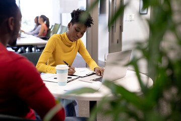 Young african american businesswoman writing on document while discussing with businessman at office