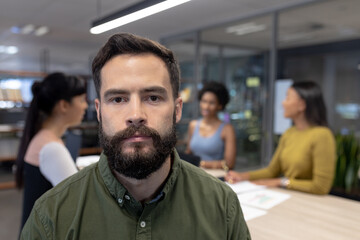 Portrait of bearded caucasian male advisor against team at modern workplace