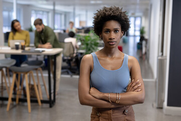 Portrait of confident young african american businesswoman standing with arms crossed at workplace