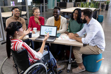Disabled biracial businesswoman explaining strategy to happy colleagues during meeting - Powered by Adobe