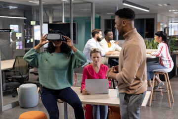 Hispanic businesswoman discussing with african american businesswoman wearing vr headset in meeting