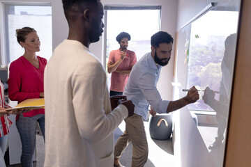 Caucasian businessman writing strategy on whiteboard during meeting with multiracial colleagues