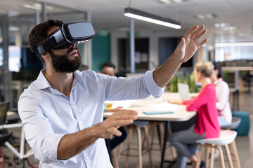 Bearded caucasian businessman gesturing while experiencing virtual reality simulator in meeting