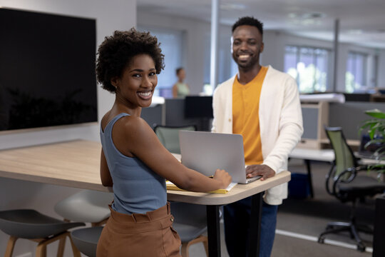 Portrait of smiling african american colleagues with laptop on desk working together in office