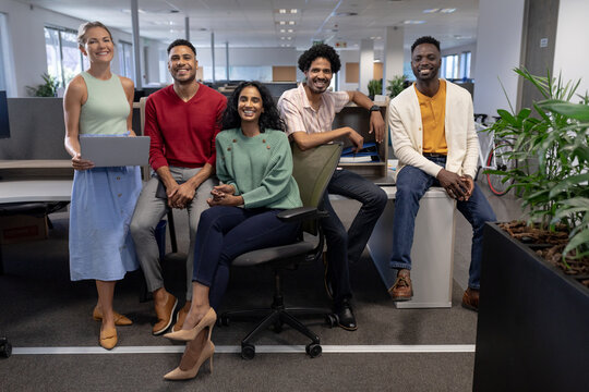 Full length portrait of smiling multiracial male and female advisors at modern workplace
